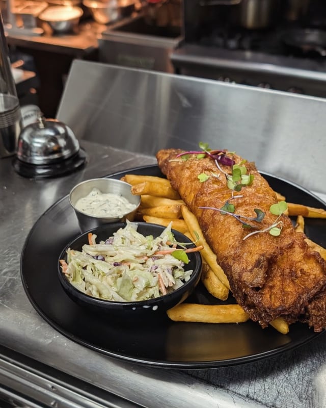 Beer-battered fish and chips with slaw on a black plate in the kitchen