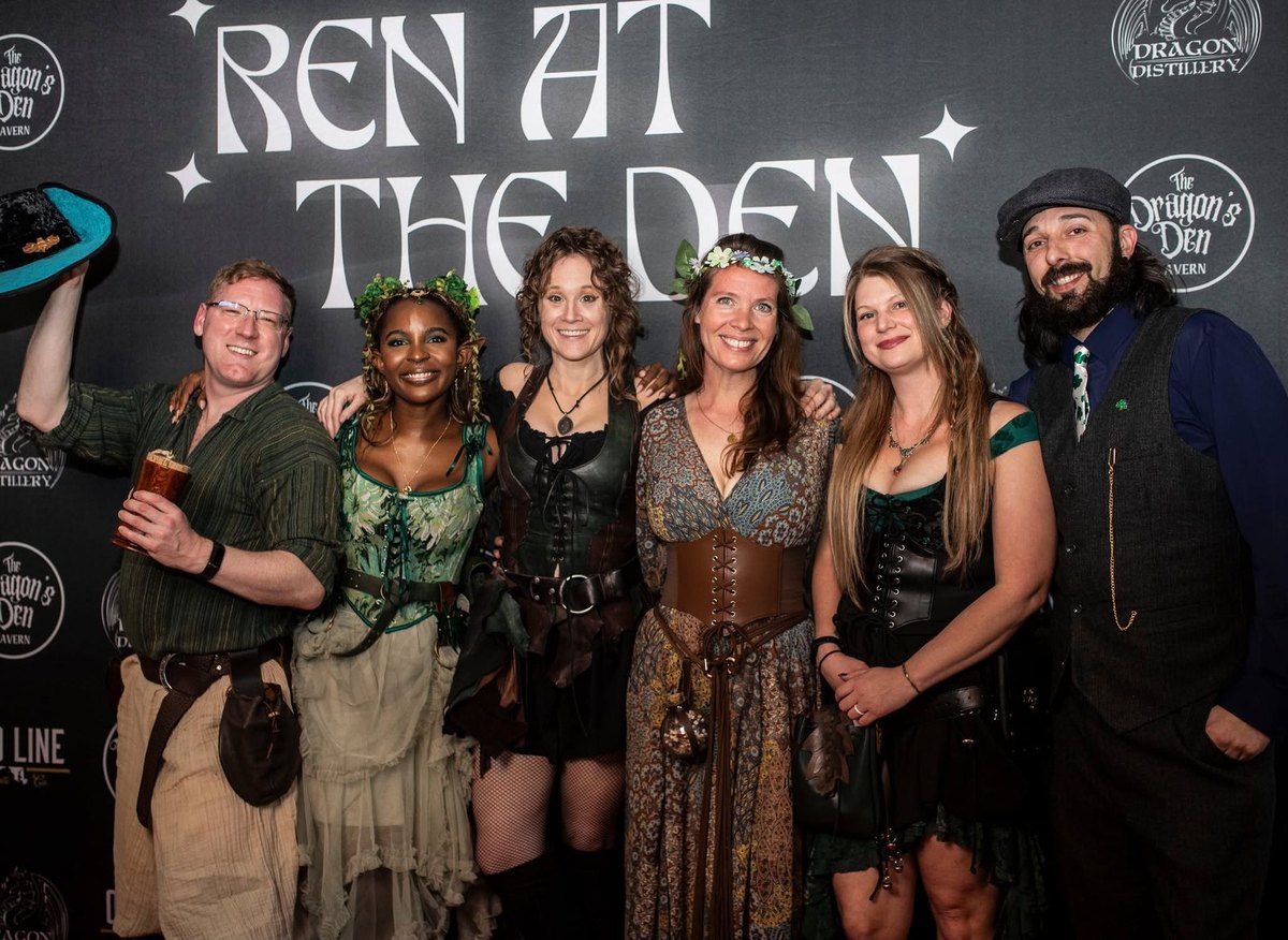 A Ren at the Den night: six guests in costume in front of the Ren at the Den backdrop at The Dragon's Den Tavern