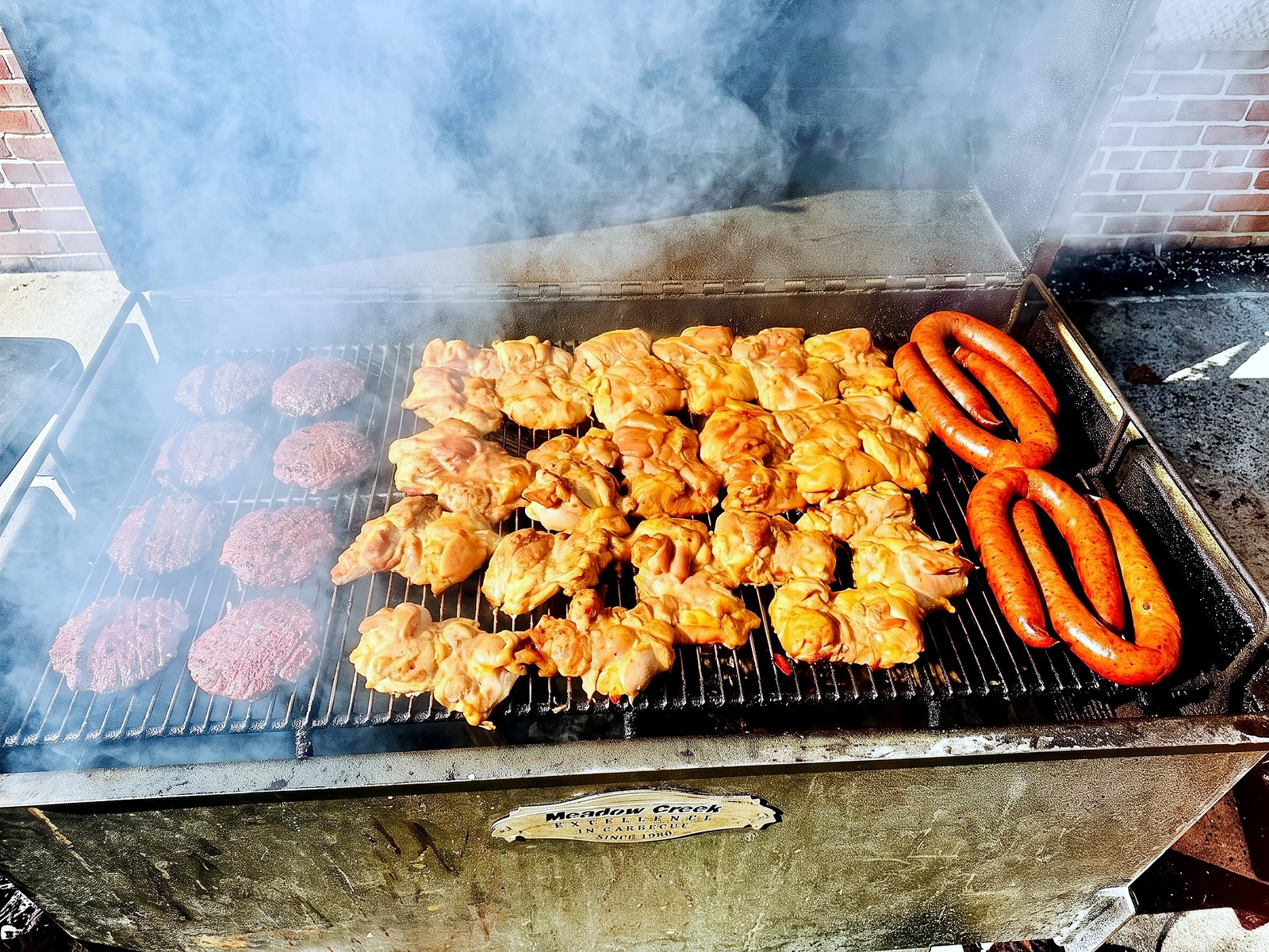 Burgers, chicken thighs and sausage on the grill in a cloud of smoke