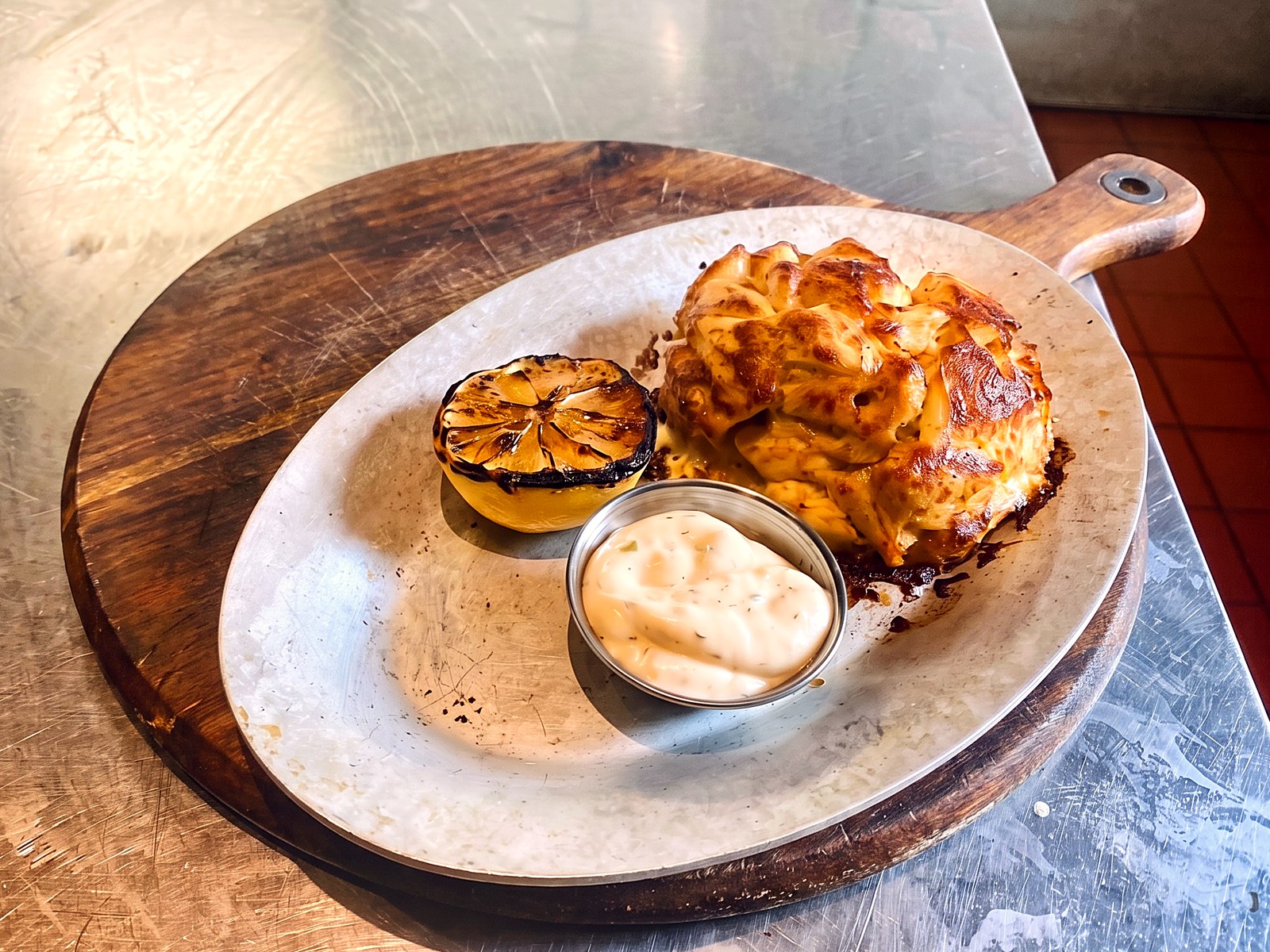 A broiled jumbo-lump Maryland crab cake with charred lemon on a dark wooden board