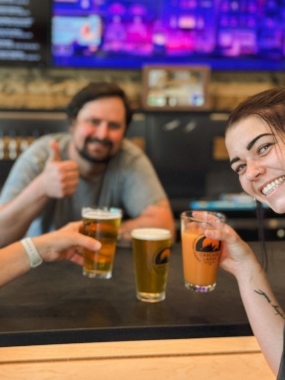 Three pints raised over the bar at Dry Canyon Club, the tap board glowing behind them