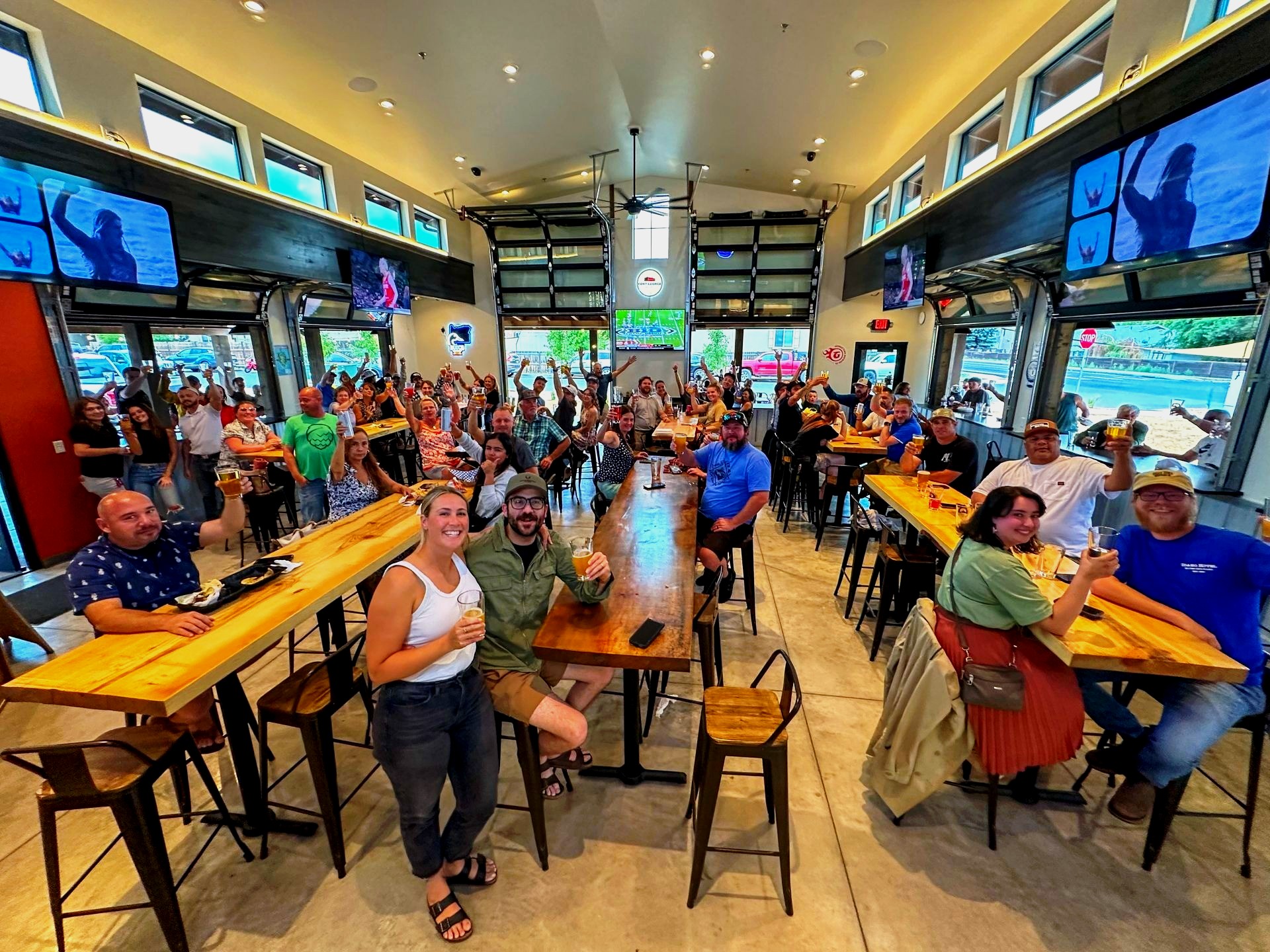 A packed room at Dry Canyon Club – full communal tables, raised glasses, garage doors open to the street